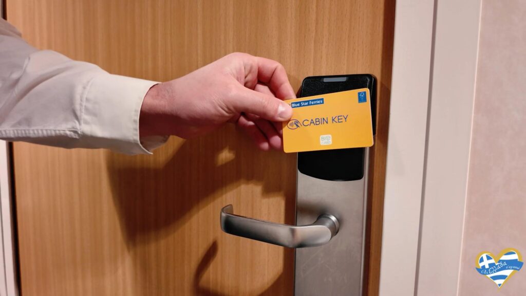 Hand inserts a yellow CABIN KEY card into a door lock on a wooden door (hotel/ship cabin).