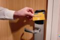 Hand inserts a yellow CABIN KEY card into a door lock on a wooden door (hotel/ship cabin).
