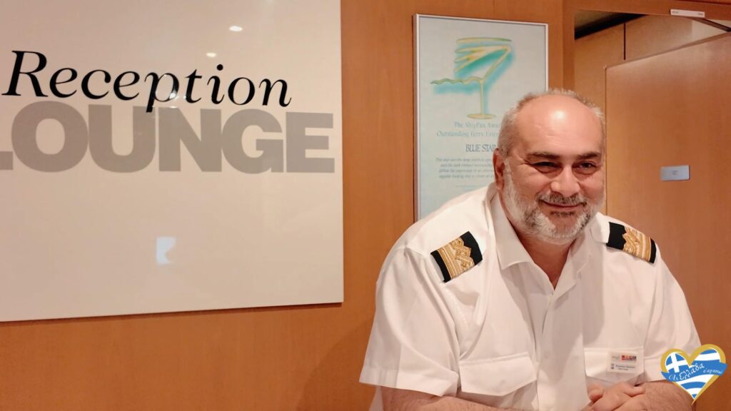 Smiling hotel receptionist in a white uniform with shoulder epaulets at a front desk beside a large'Reception' sign. (Informative)