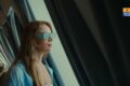 Woman wearing turquoise 3D-style glasses gazing out the ferry window, Blue Star Ferries logo in the top-right corner