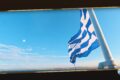 Blue and white Greek flag waving on a mast against a clear blue sky over the sea horizon