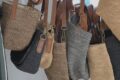 Assortment of woven straw tote bags with leather straps hanging together.