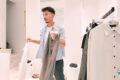Man shopping in a bright clothing store, holding a white shirt and a pair of gray pants near a rack of clothes.