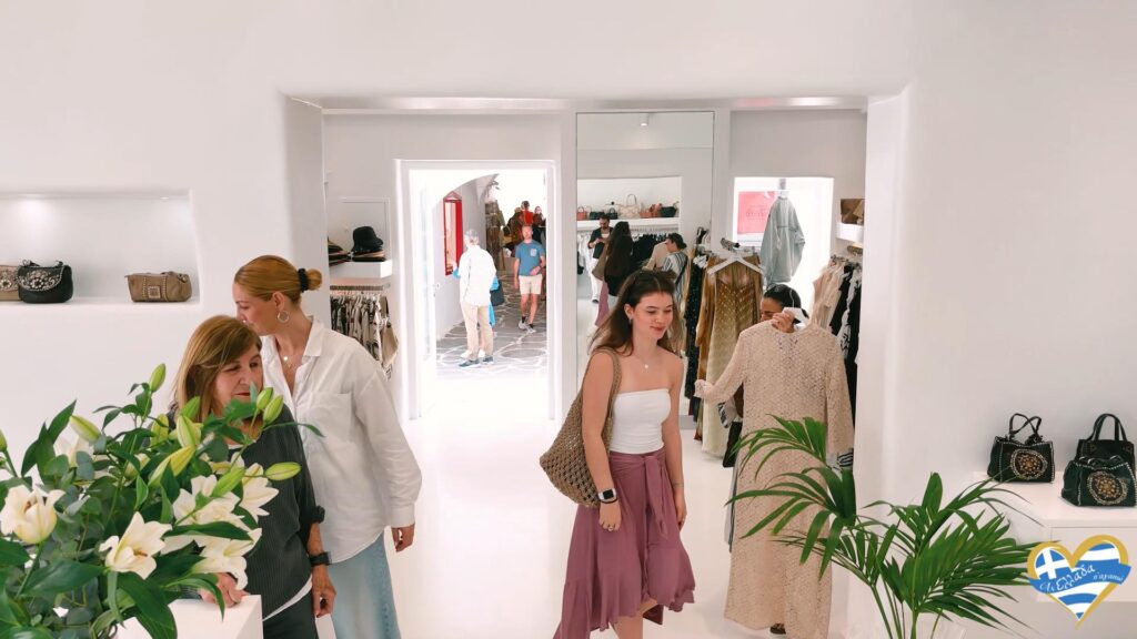 Shoppers browse clothes in a bright white boutique with handbag displays and plants in the foreground.