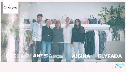 Five people stand together in a fashion boutique with clothing racks and handbags behind them.