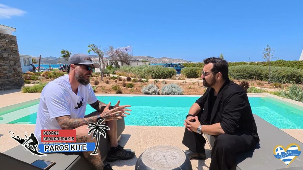 Two men sit and chat beside a bright turquoise pool on a sunny day, outdoor garden setting, with Paros Kite logos in the corner.