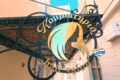 Decorative wrought-iron sign with a teal-yellow abstract head silhouette and Greek text on an ornate frame.