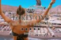 Back view of a woman with arms raised overlooking a Santorini beach club and white buildings, with promotional text 'FORTY ONE' and 'THE ULTIMATE EXPERIENCE'.