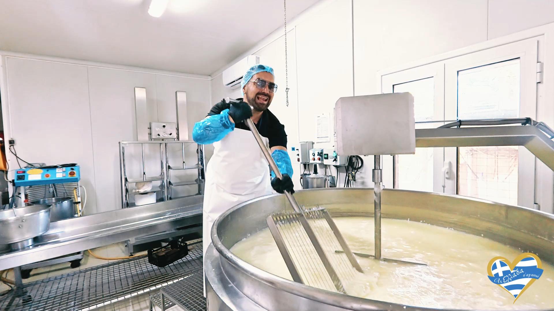Dairy plant worker wearing a hairnet, goggles, and gloves, stirring a large stainless steel milk vat with a long paddle.