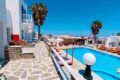 White-washed hotel courtyard with a bright blue pool, stone walkways, and orange loungers under clear skies.