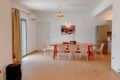 Open-plan dining area with a wooden table, six white chairs, a pendant light, wall art, and a fridge visible in the kitchen.