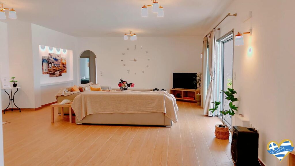 Bright living room with a beige sectional sofa, colorful cushions, and a TV on a wooden stand facing large glass doors.
