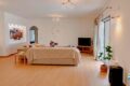 Bright living room with a beige sectional sofa, colorful cushions, and a TV on a wooden stand facing large glass doors.