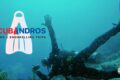 Underwater scene promoting Scubandros: a diver swimming with a camera, logo text 'SCUBANDROS DIVING & SNORKELLING TRIPS' overlaid on the left, and a heart-shaped Greek flag badge bottom right.