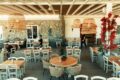 Bright cafe interior with a stone wall, wooden tables, and white chairs, large woven pendant lights, and red flowering vines.