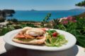 Plate with smoked-salmon Eggs Benedict and side salad on a white table, ocean view in the background.