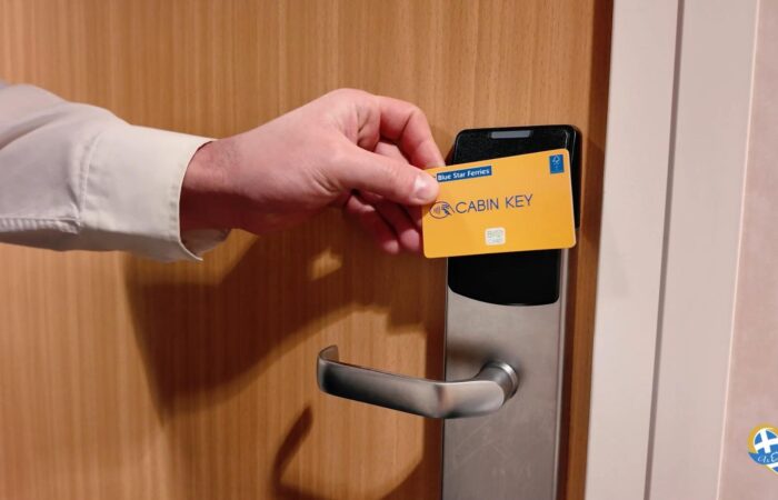 Hand inserts a yellow CABIN KEY card into a door lock on a wooden door (hotel/ship cabin).