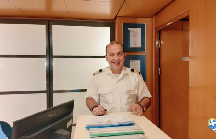 Smiling man in a white uniform with shoulder epaulettes behind a reception desk in a modern office.