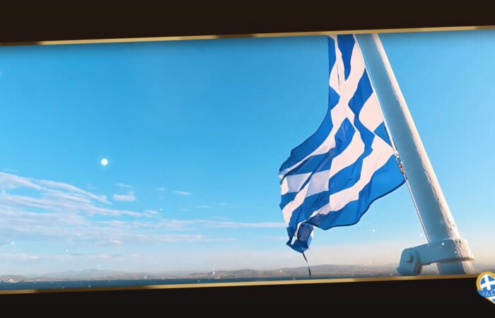 Blue and white Greek flag waving on a mast against a clear blue sky over the sea horizon