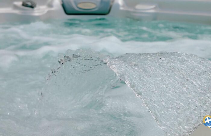 Close-up of a large clear ice chunk resting on a spa pool, with frothy water in the background and a circular logo in the bottom-right corner.