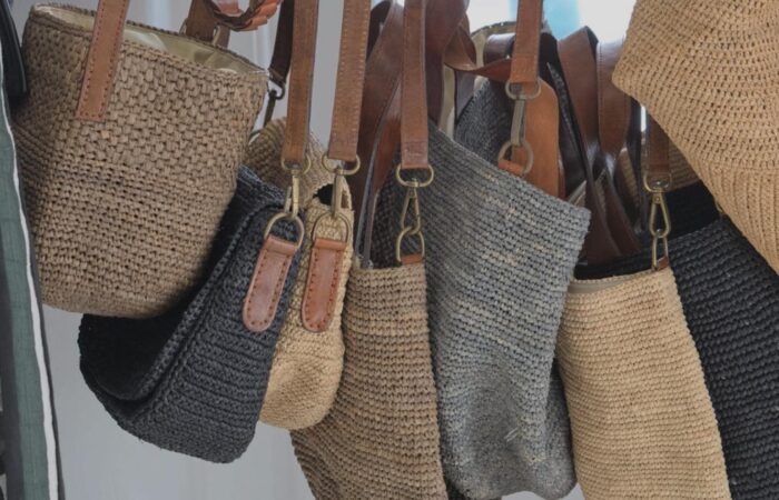 Assortment of woven straw tote bags with leather straps hanging together.