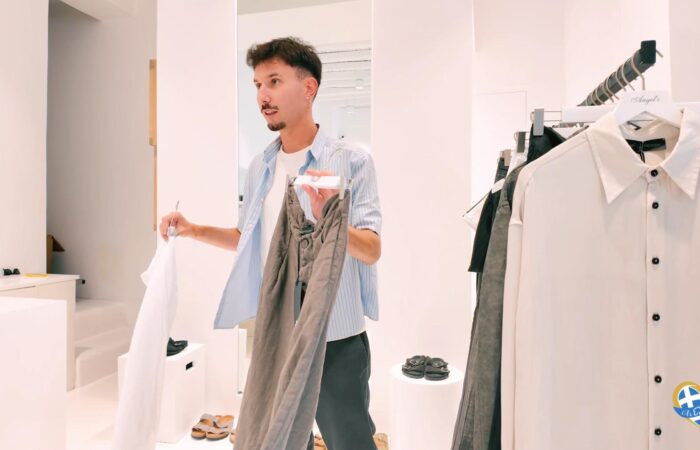 Man shopping in a bright clothing store, holding a white shirt and a pair of gray pants near a rack of clothes.