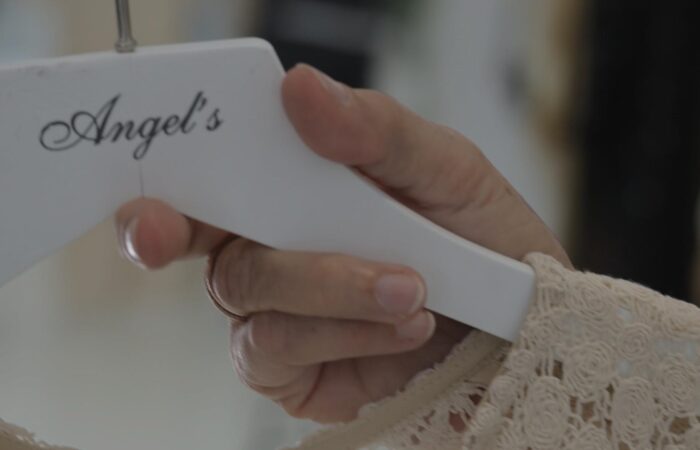 Close-up of a hand guiding a white sewing tool with 'Angel's' logo, stitching lace fabric.