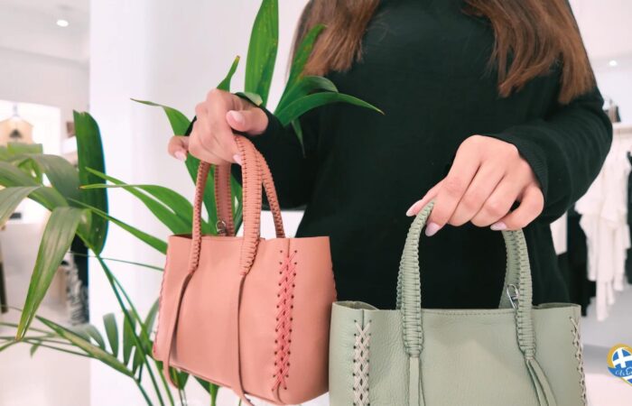 Person in a dark sweater holds two pastel handbags (pink and mint green) with woven handles in a bright shop.