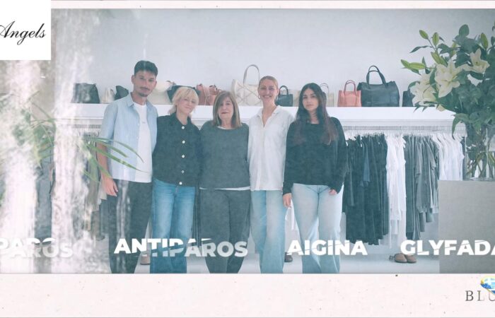 Five people stand together in a fashion boutique with clothing racks and handbags behind them.