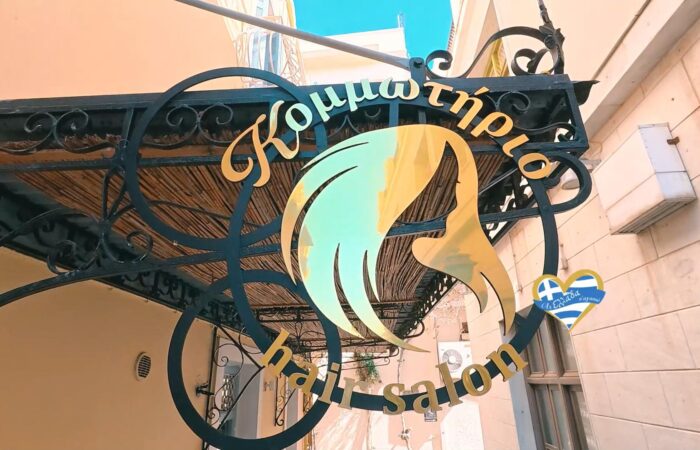 Decorative wrought-iron sign with a teal-yellow abstract head silhouette and Greek text on an ornate frame.