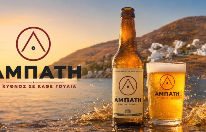 Beer advertisement banner featuring a bottle and glass of Amphati beer on a rocky shoreline at sunset with splashing water and a coastal town in the background