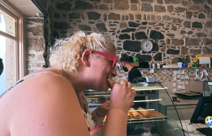 Woman with red glasses biting into a pastry at a bakery counter.