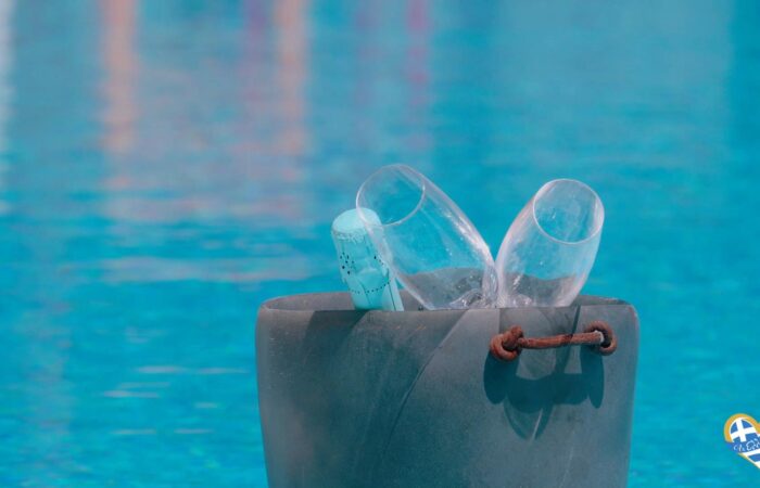 Bucket holds two broken glass bottles against a blue ocean backdrop, highlighting beach cleanup.